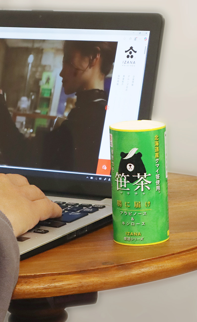 落ち着いた壁紙を背景に木目のテーブルがあり、お盆に乗ったガラスのコップに笹茶が注がれている様子が見える。透明感のある雰囲気が感じられる。